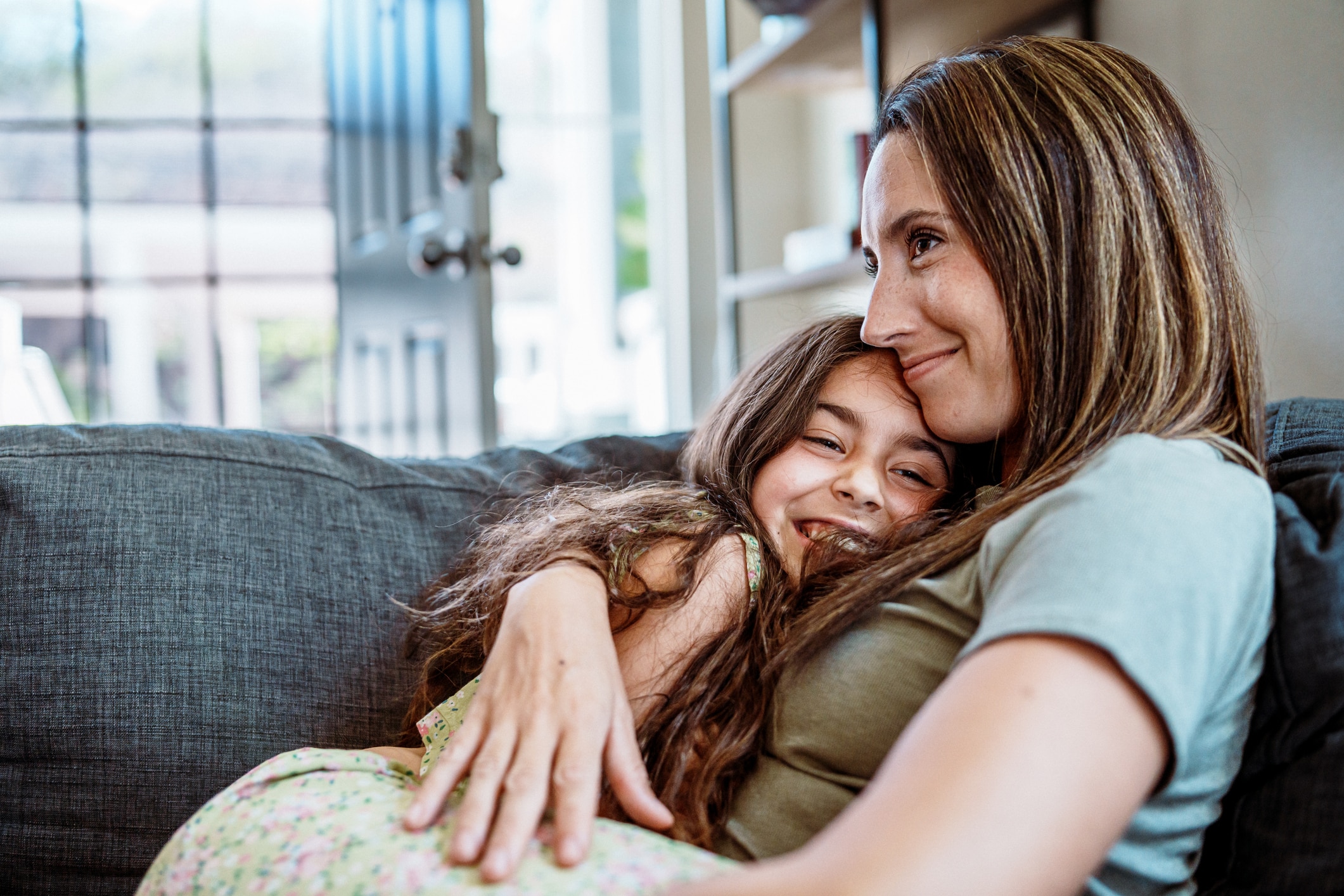 Young girl and mother hug each other on the couch