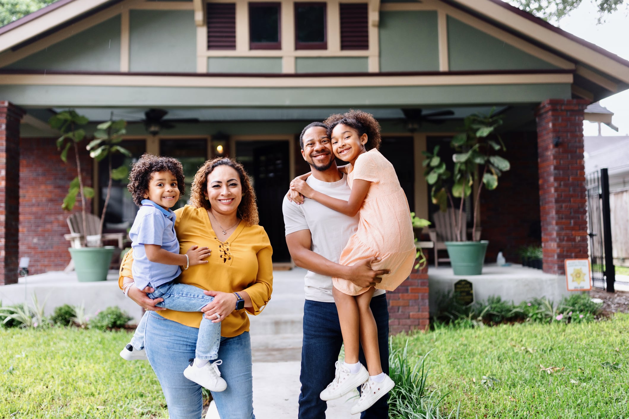 Portrait of multiracial parents holding their kids in front of the house